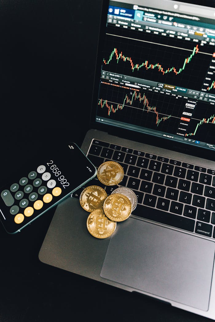 OLE777 A still life of Bitcoin coins, a smartphone calculator, and a trading chart on a laptop.